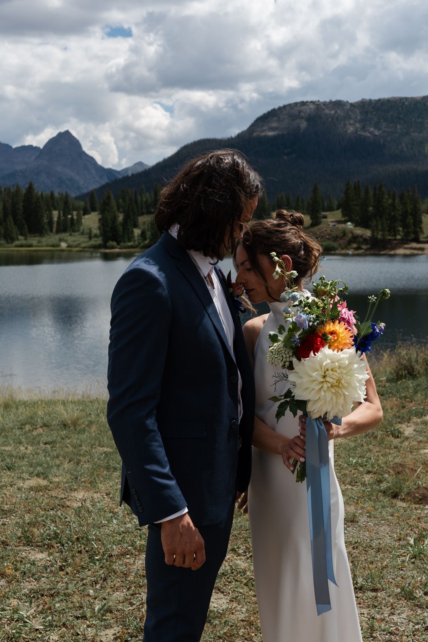 Romantic couple sharing intimate moment by mountain lake with stunning floral bouquet.