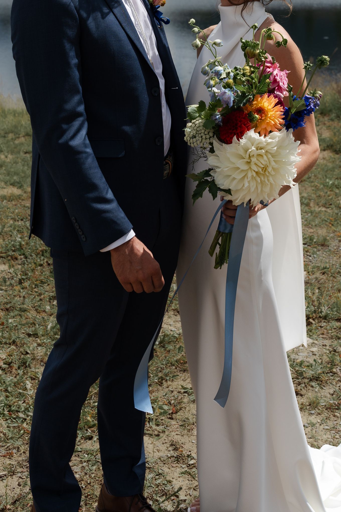 Close-up of newlyweds showing navy suit and white dress with colorful dahlia bouquet.