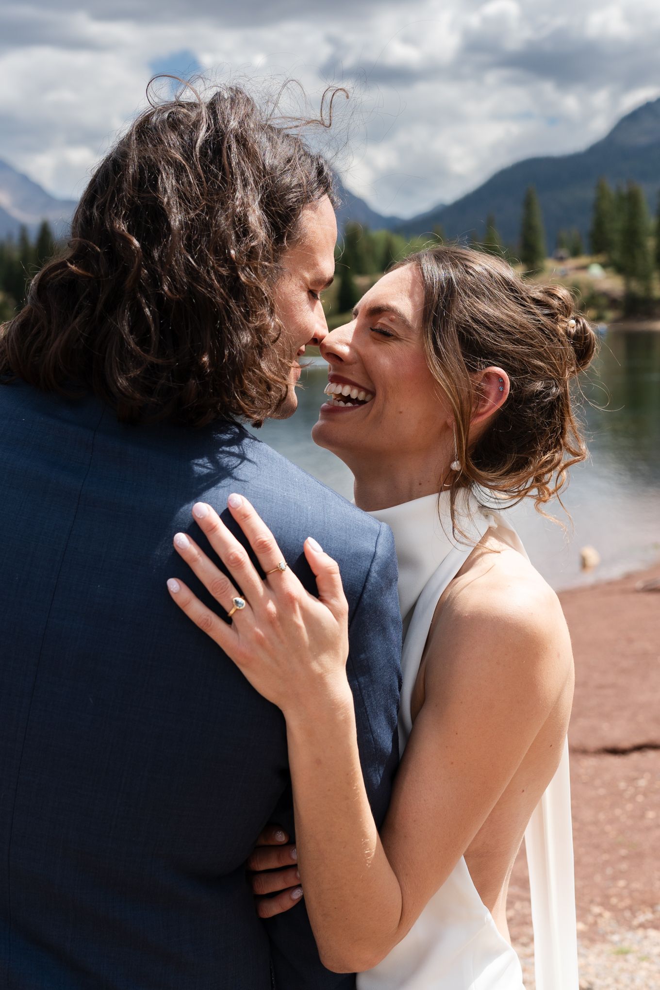 A romantic moment between a couple by a mountain lake with cloudy skies in the background.
