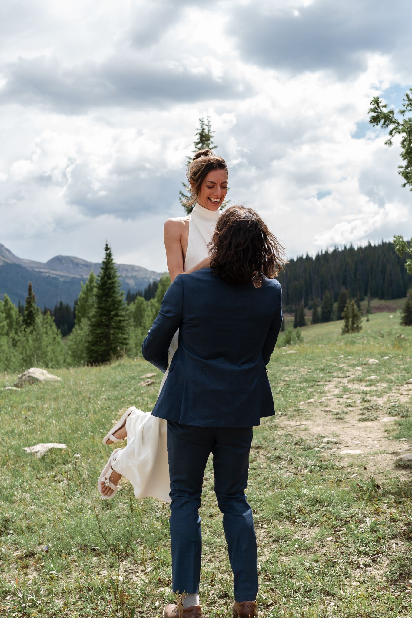A joyful wedding moment captured in mountain meadow with dramatic cloudy sky.
