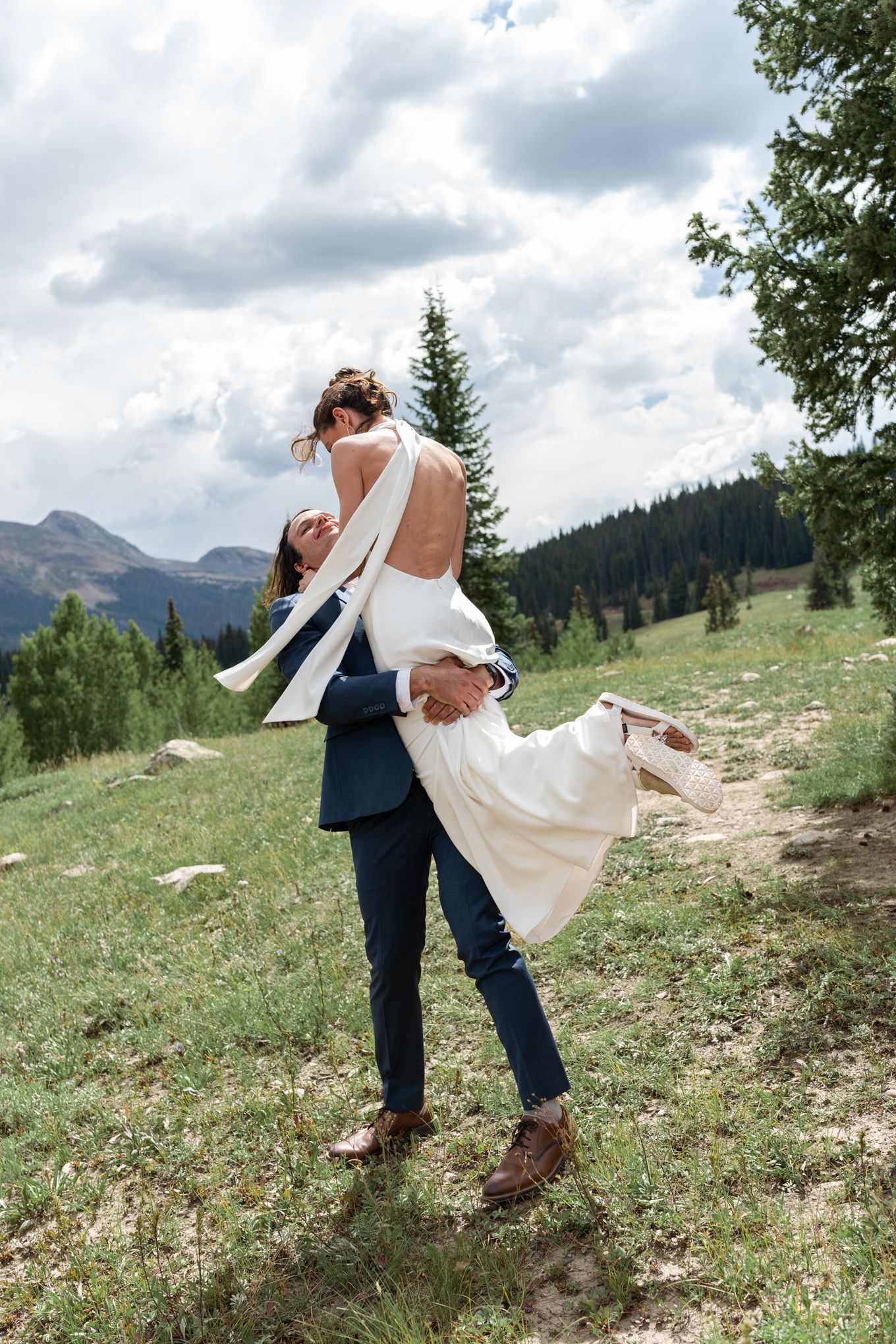 A romantic lift pose against mountain landscape with dramatic clouds and pine trees.