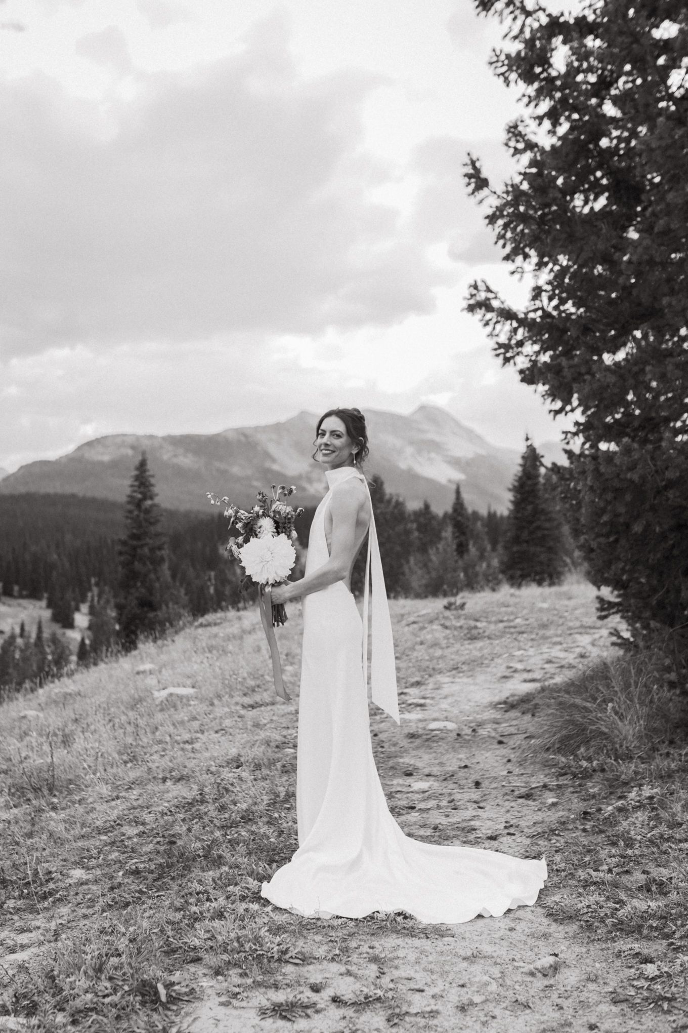Black and white portrait of bride with bouquet against dramatic mountain landscape.