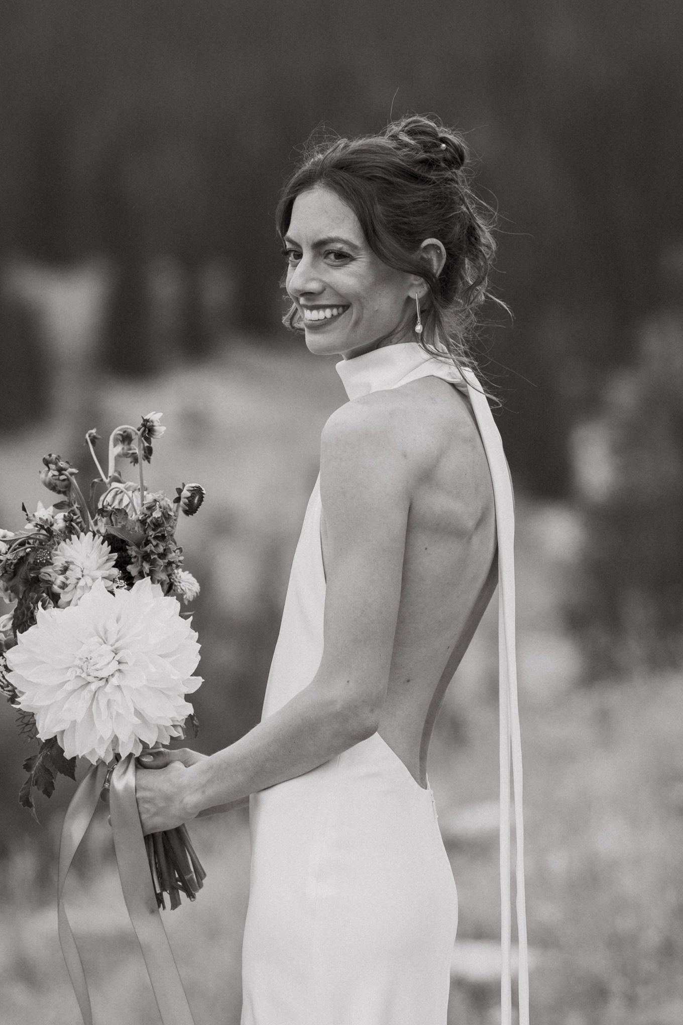Elegant backless wedding dress detail with bride holding floral bouquet in black and white.