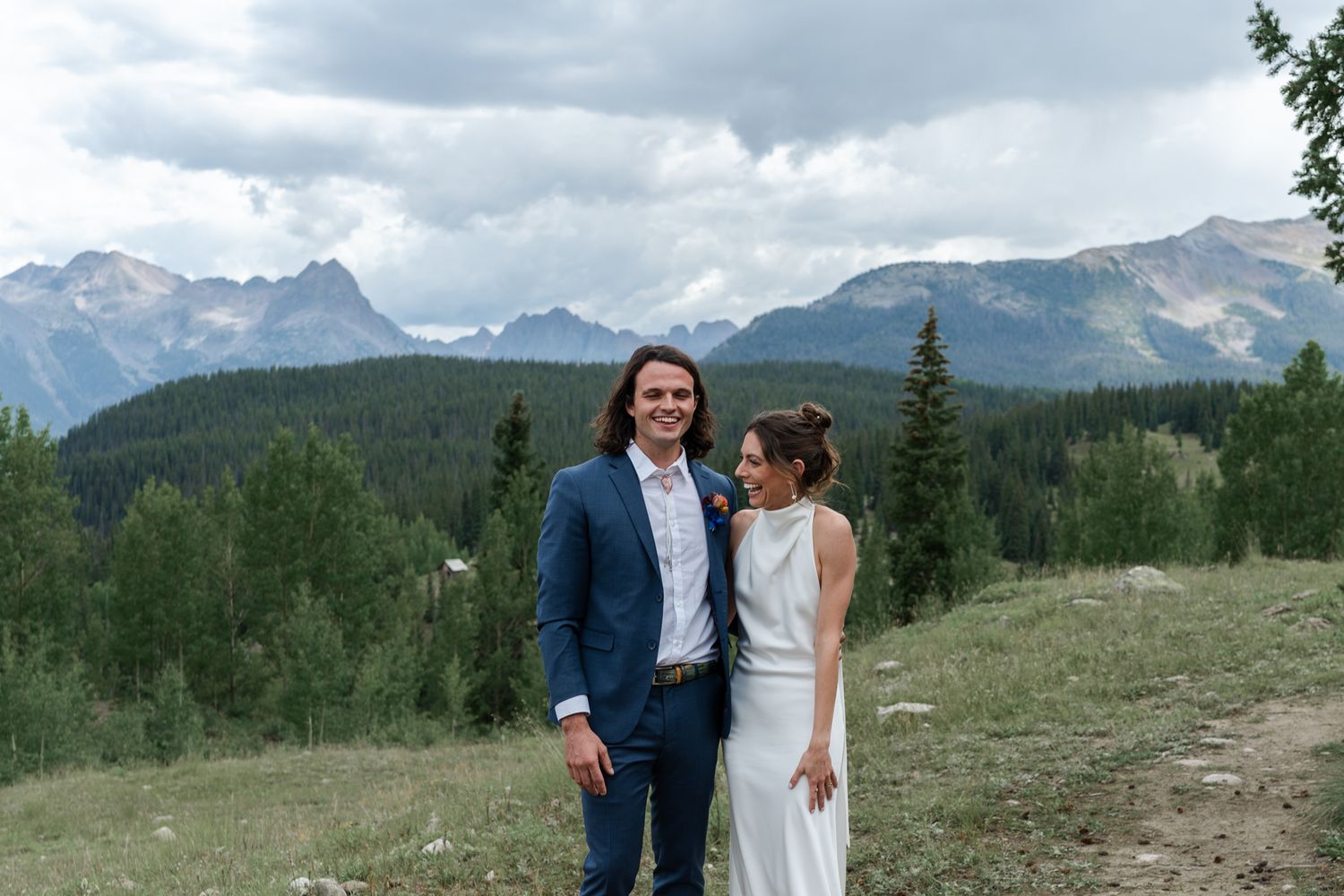 Wedding couple share an intimate moment while standing in the mountains surrounded by evergreen trees.