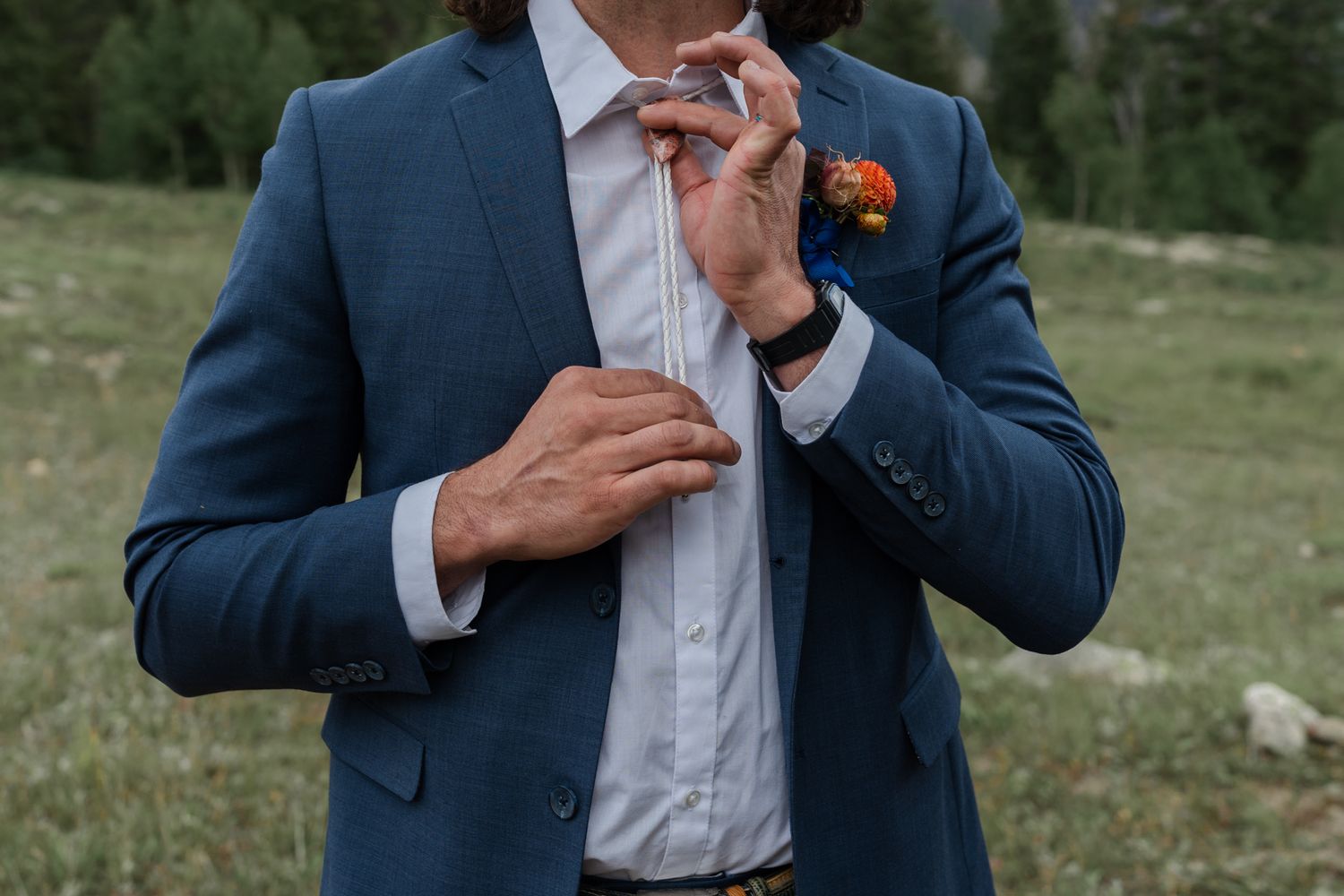 Close-up detail of navy suit jacket with orange boutonniere and bow tie adjustment.
