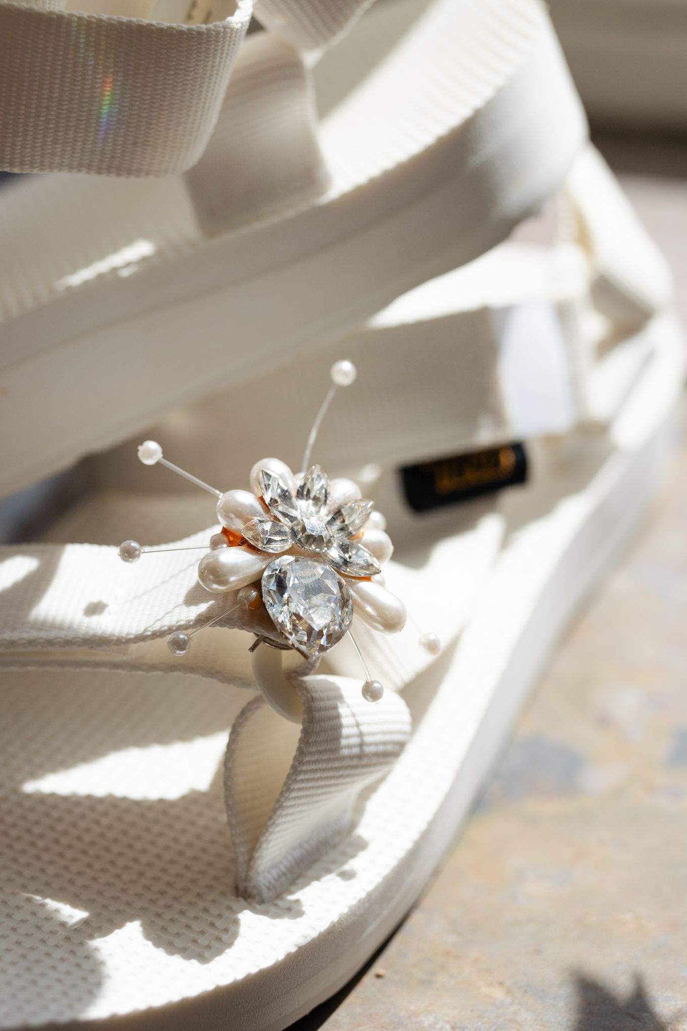 Crystal embellished white sandal with decorative pins in bright natural light.