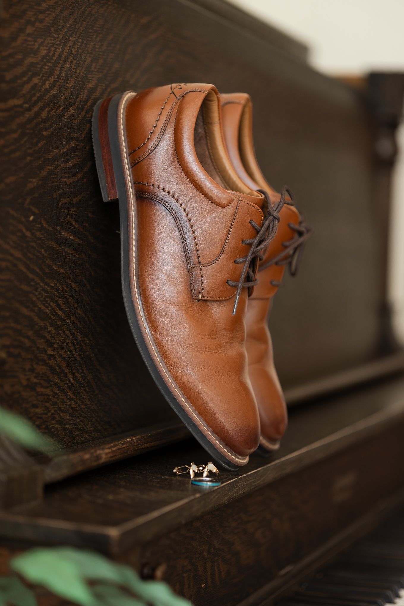 Brown leather dress shoes with wedding rings placed on wooden surface.