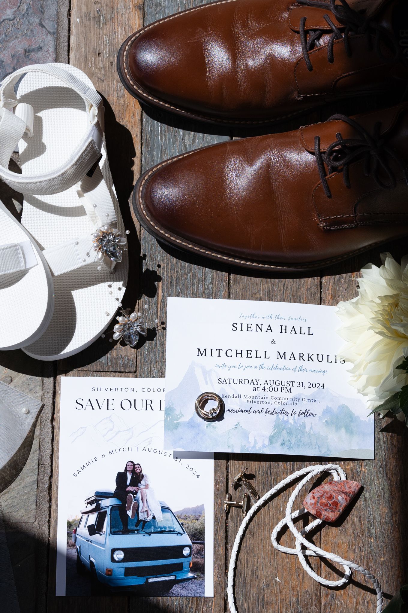 Wedding invitation cards and brown leather shoes on wooden deck in sunlight.