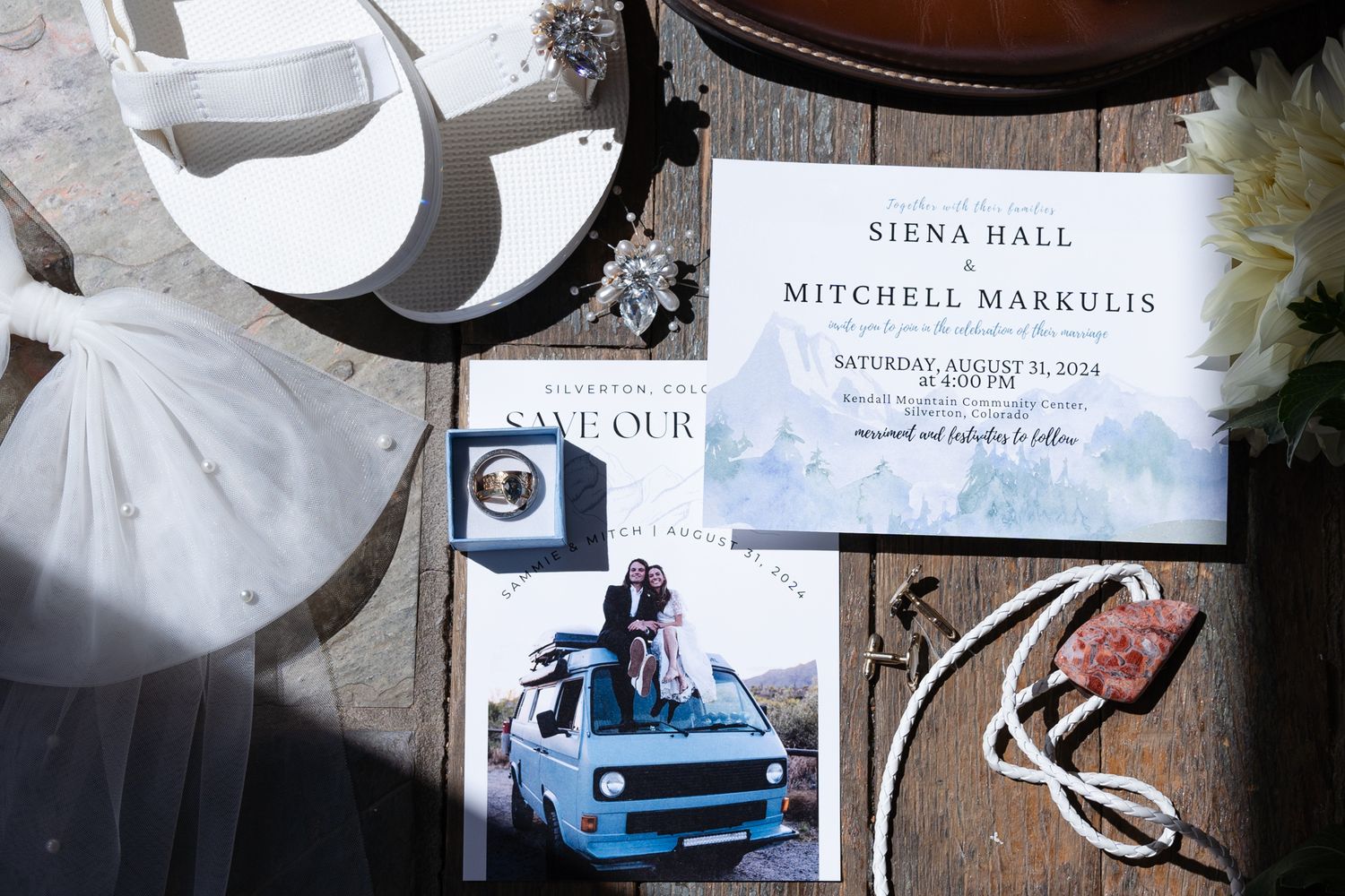 Wedding invitation and details flat lay featuring blue car photo and decorative elements on a textured surface.