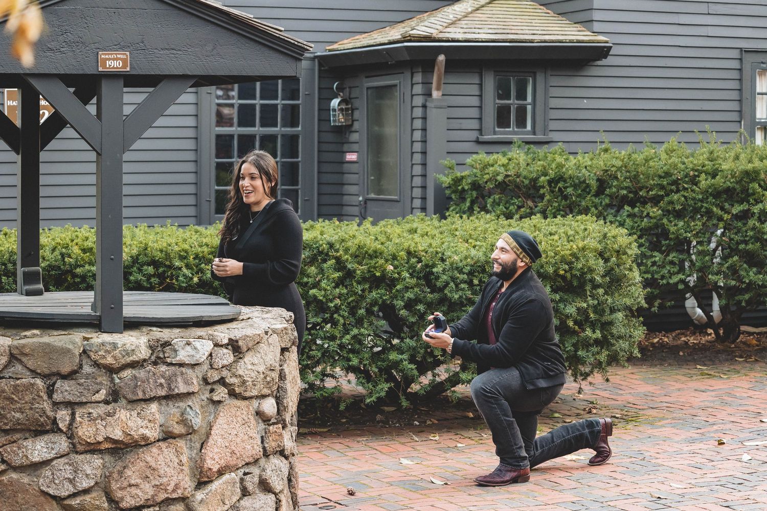 A proposal scene with someone kneeling on brick pavement in front of a stone wall.