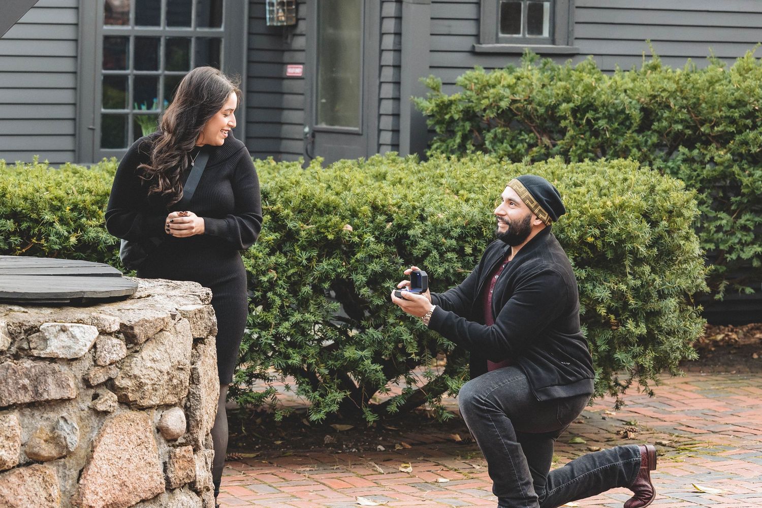 A surprise proposal moment captured outside a gray house with traditional architecture.