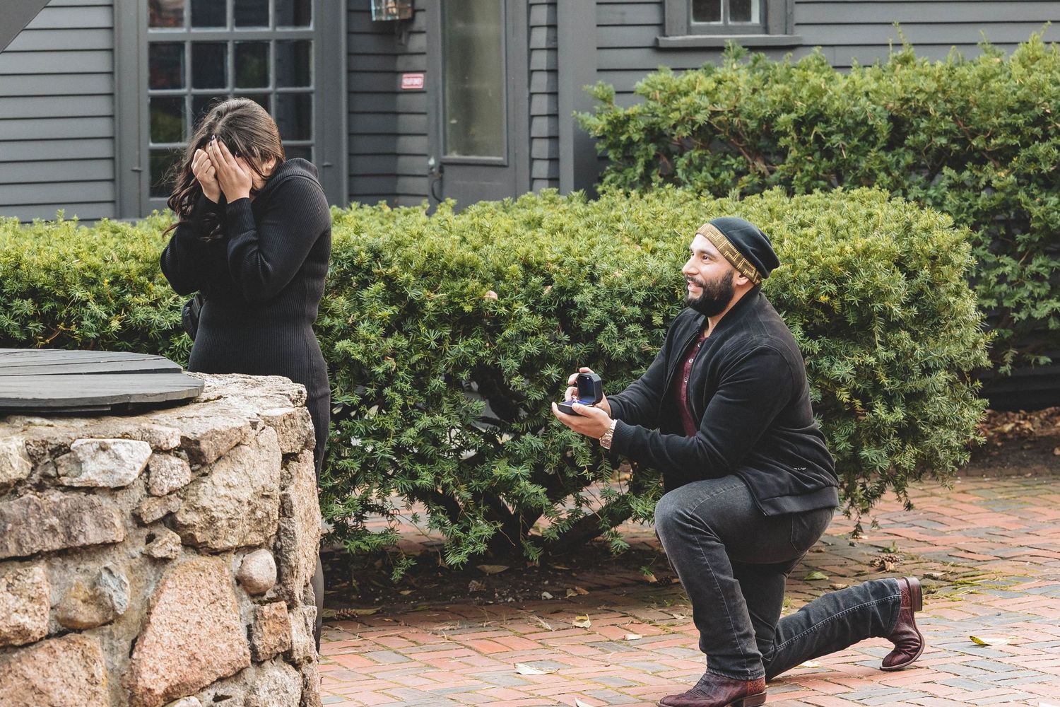 An emotional reaction during a surprise proposal outside a traditional gray house.