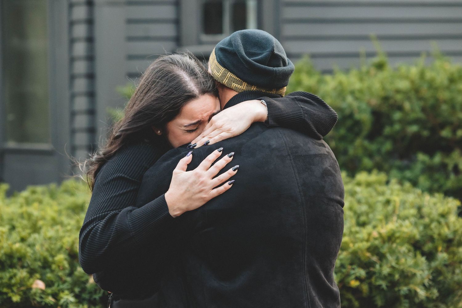 Two people share an intimate hug outdoors near a residential building.