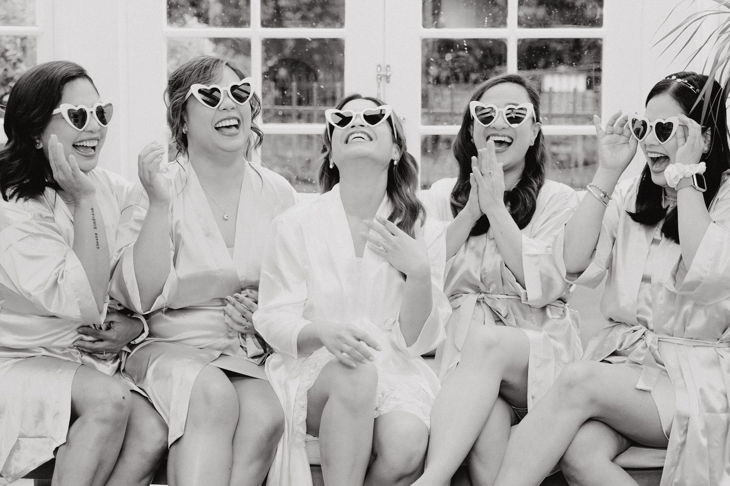 A photo of a group of people in white robes and sunglasses laughing together captured by Apertured Media Auckland Wedding Photographer.