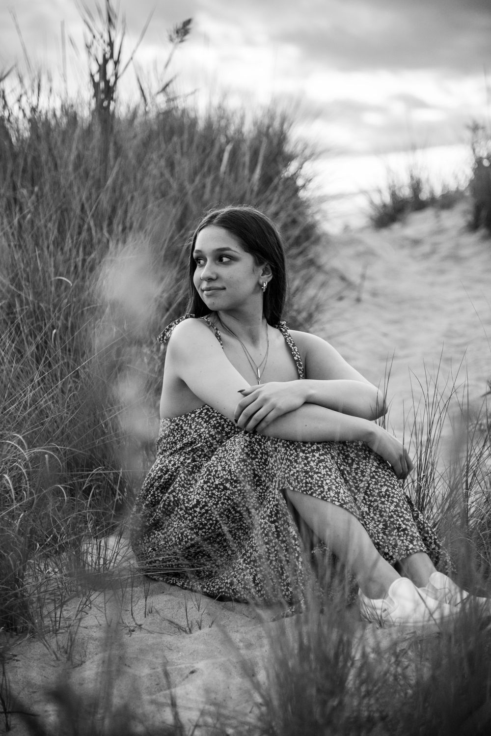 Black and white portrait of someone sitting thoughtfully among beach grass on sand dunes at twilight.