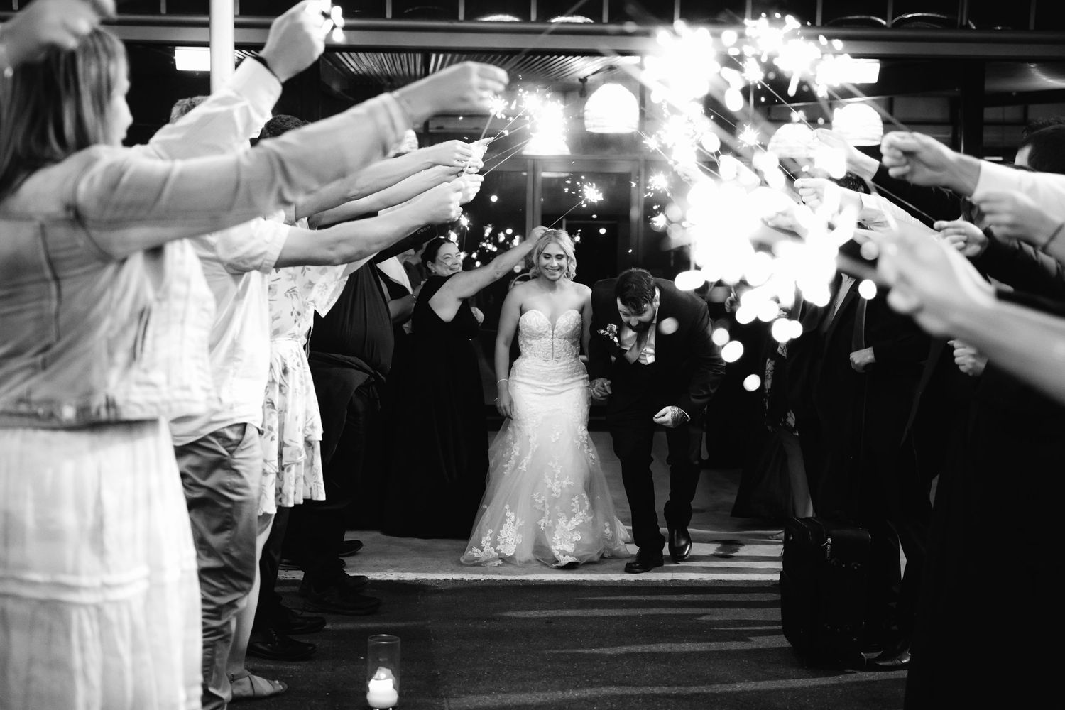 Black and white wedding photo with sparklers creating light trails during couple's exit.