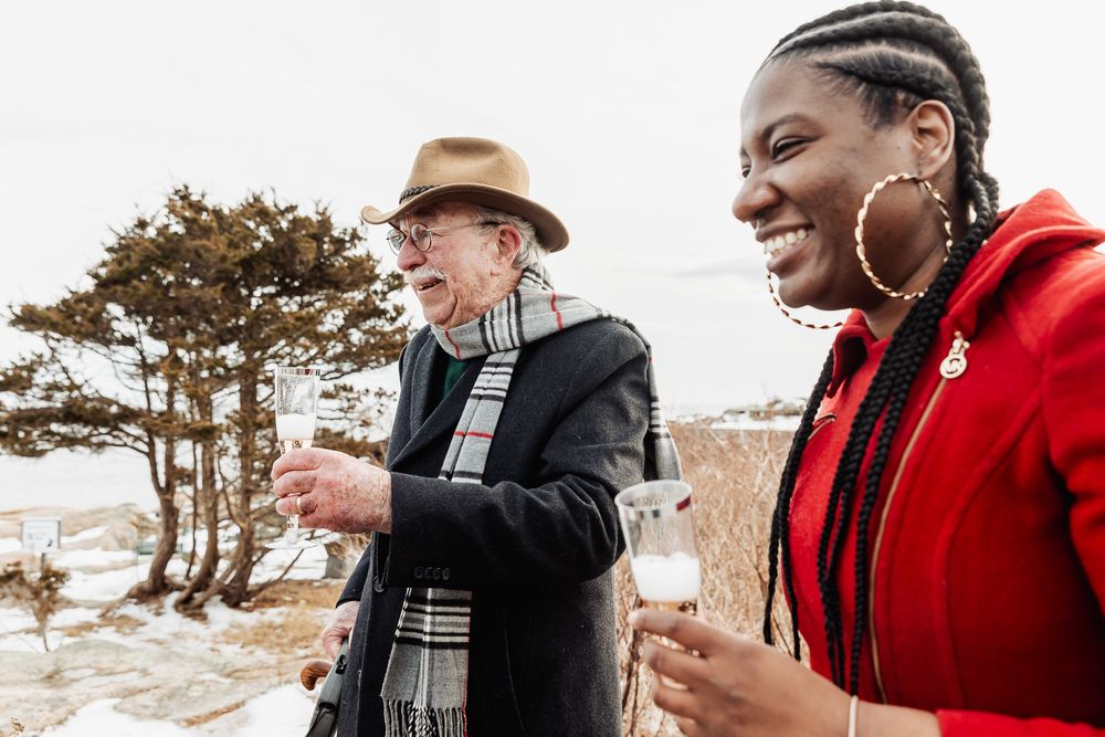 Two people share a laugh while enjoying coffee outdoors on a chilly winter day near the coast.