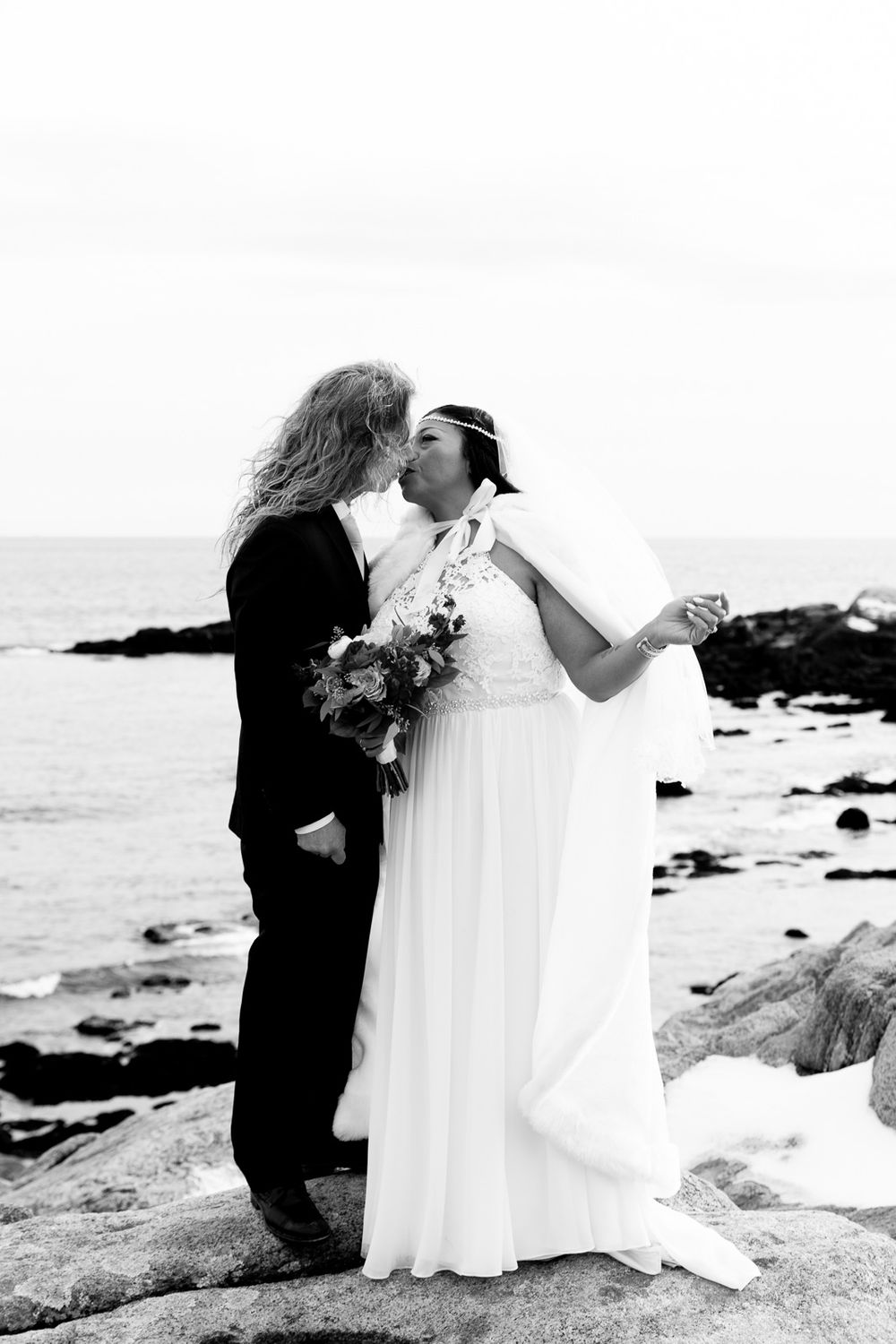 A romantic black and white wedding photo captured on a rocky ocean coastline.