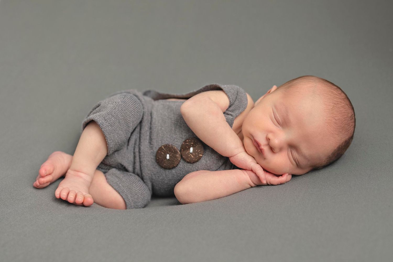Sleeping baby in gray romper lies on gray background. Newborn baby photographer in Gosport, baby photography in Hampshire studio, fareham