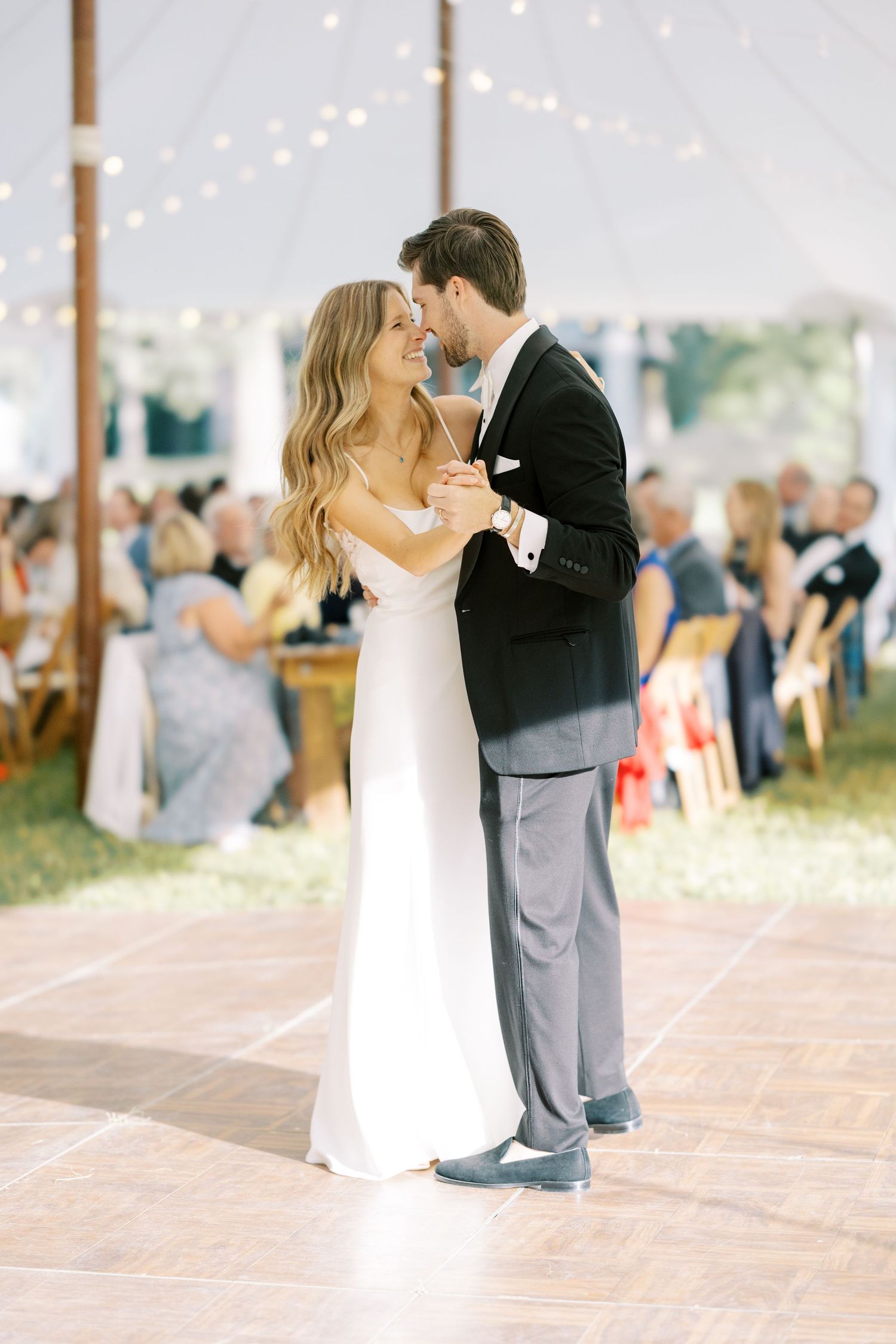 Newlyweds share a romantic first dance on a rustic wooden dance floor under a tent at their wedding reception.
