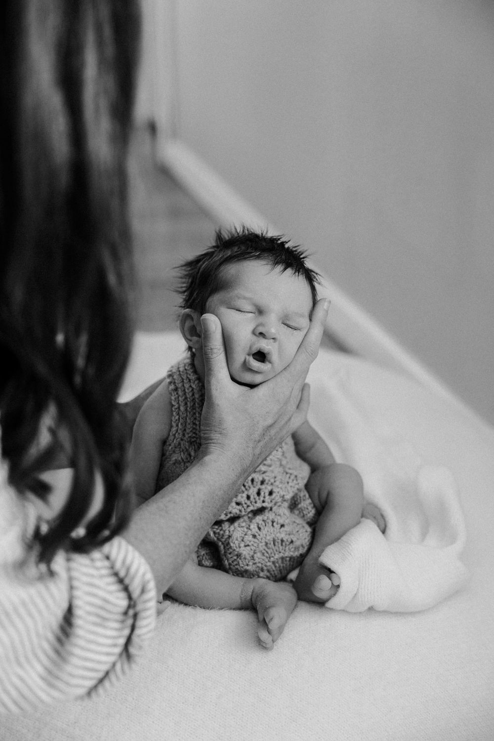 A newborn baby yawning while being cradled in black and white photography.
