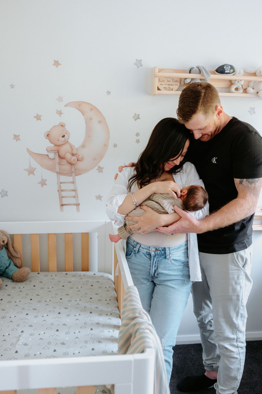 Family standing in a nursery decorated with whimsical moon and star wall decals beside a white crib.