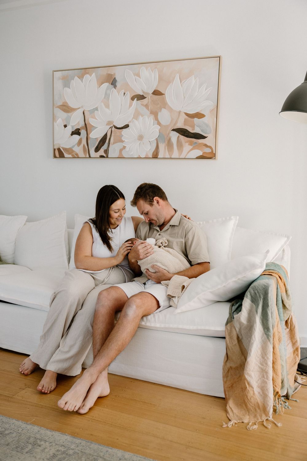 A cozy living room scene with two people relaxing on a white couch beneath floral wall art.
