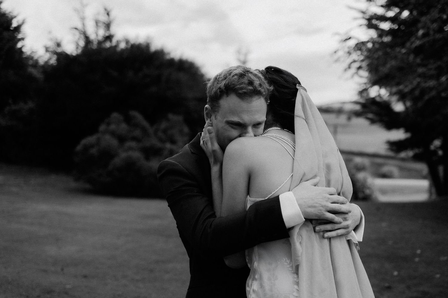 A tender moment between newlyweds embracing outdoors in black and white photography.