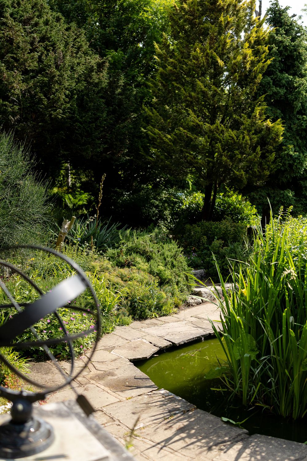 Stone pathway leads through a lush garden with a decorative sundial and water feature in the foreground.
