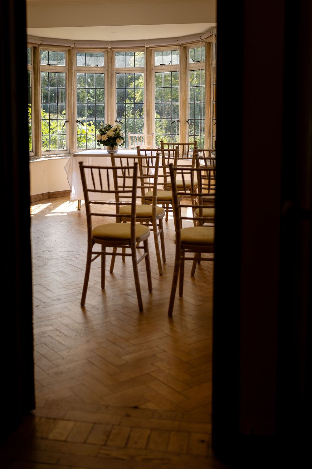 Elegant bay window room with wooden chairs arranged in rows and herringbone hardwood flooring.