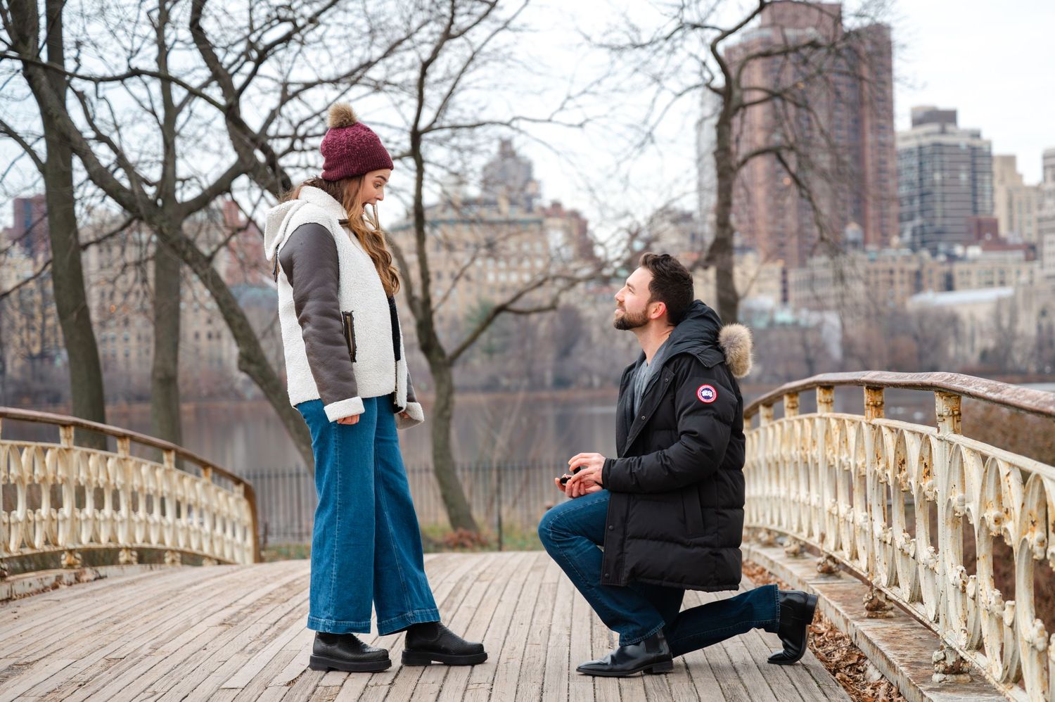 A romantic proposal moment takes place on a the Gothic Bridge in Central Park with the New York City skyline in the background.