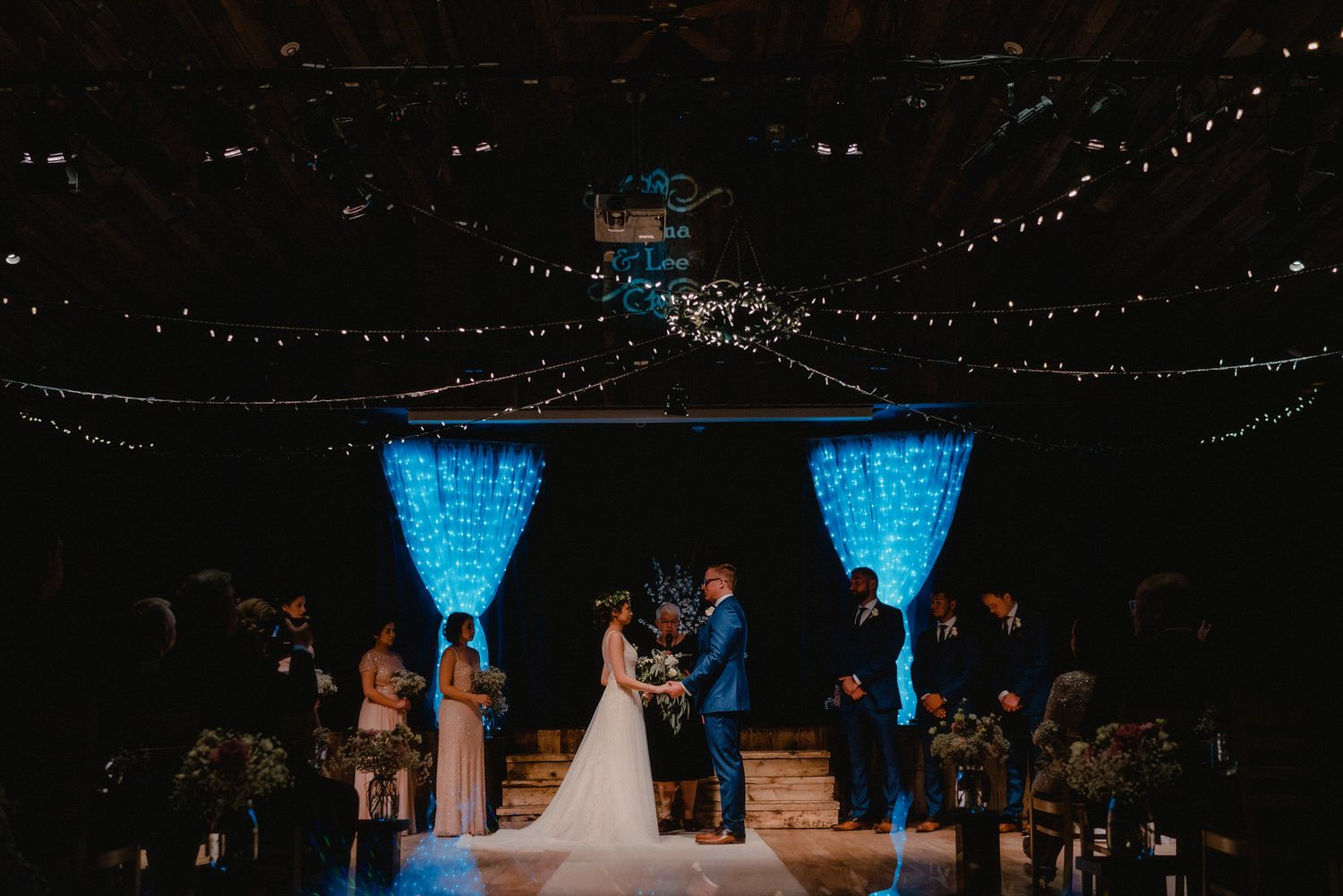 Romantic wedding ceremony at Cornerstone Theatre in Canmore, featuring elegant decor, bridal party, and heartfelt vows under twinkling light