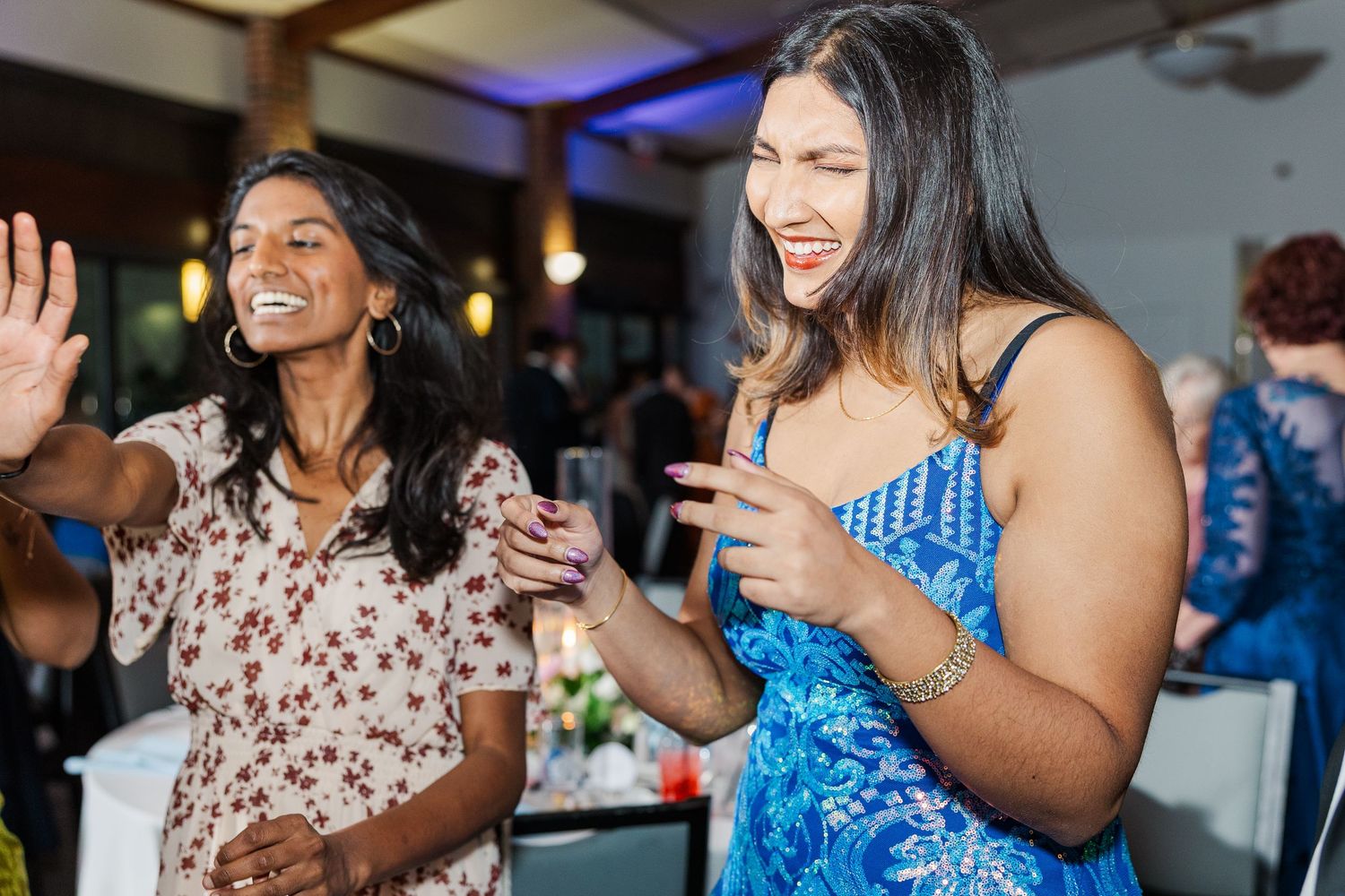 Two people in festive attire dance and laugh while enjoying themselves at an indoor social gathering.