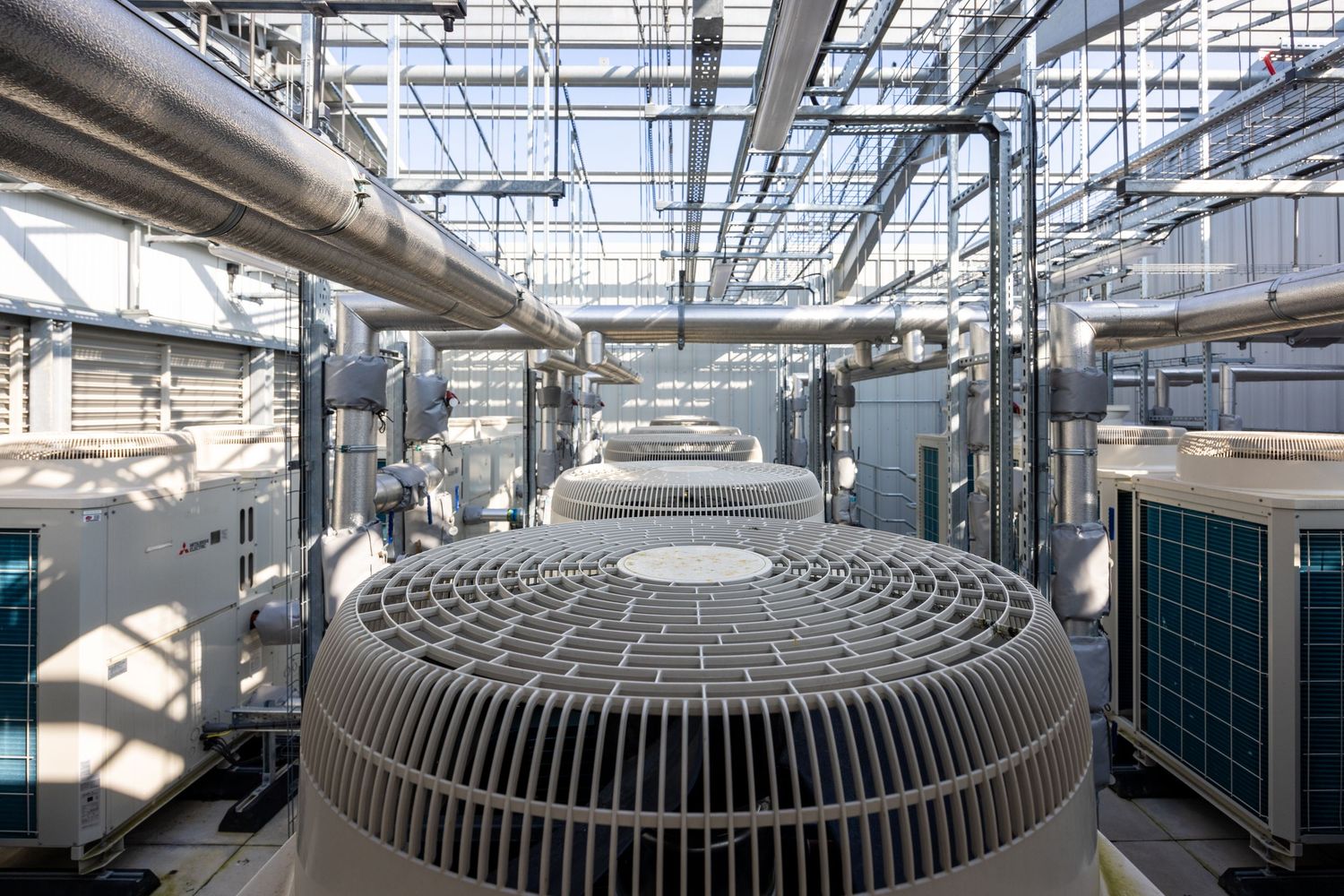 Large industrial cooling fan unit surrounded by HVAC equipment and piping.