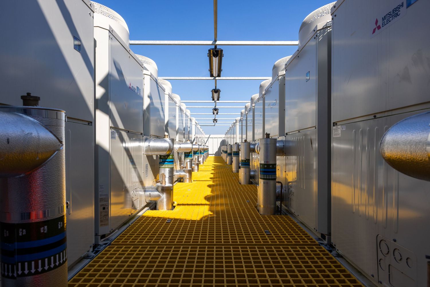 Industrial walkway with yellow grating floor and white equipment installations along both sides.