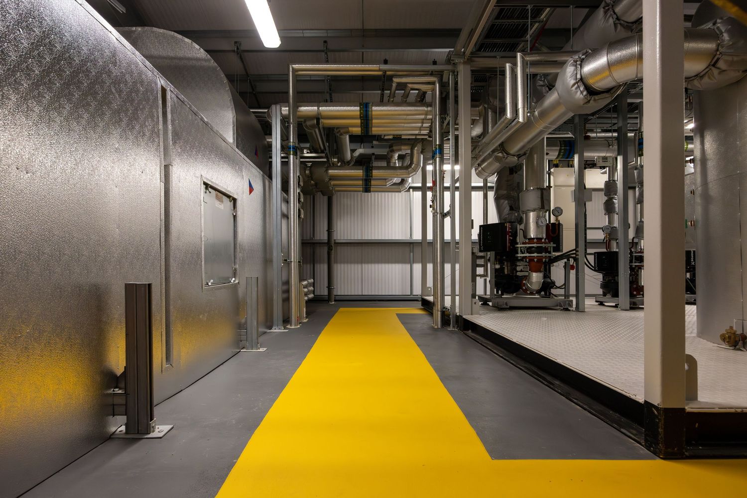 Industrial facility corridor with yellow safety walkway and metallic equipment installations.