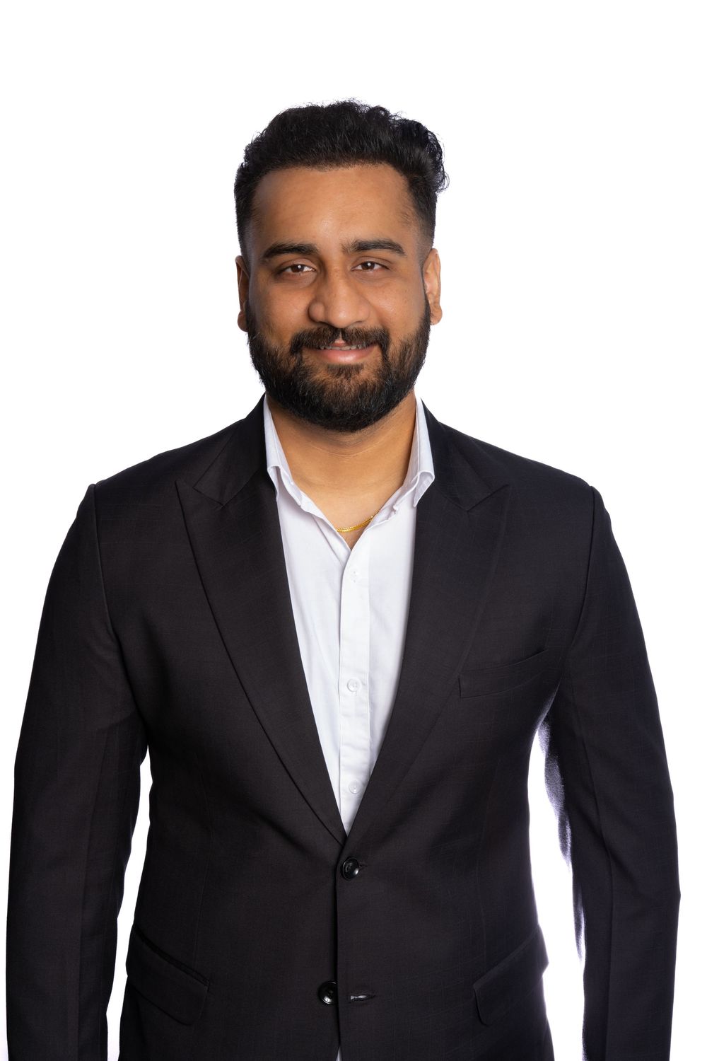 Professional headshot of a person in a black suit and white shirt smiling warmly against a white background.