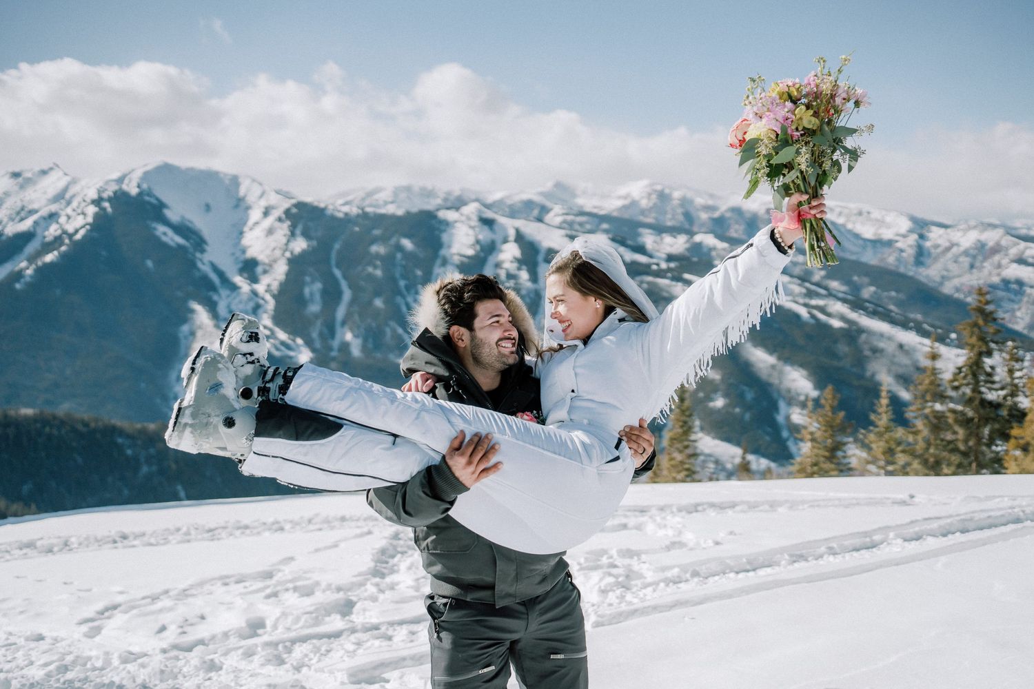 Couple enjoying a winter escape in snow-covered mountains with stunning alpine peaks and sunny skies as backdrop.