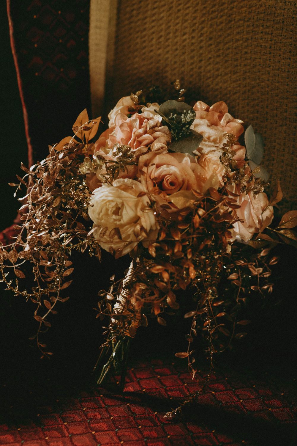 Delicate pink roses and dried floral arrangements create a moody, vintage-inspired still life in warm tones against a dark backdrop.