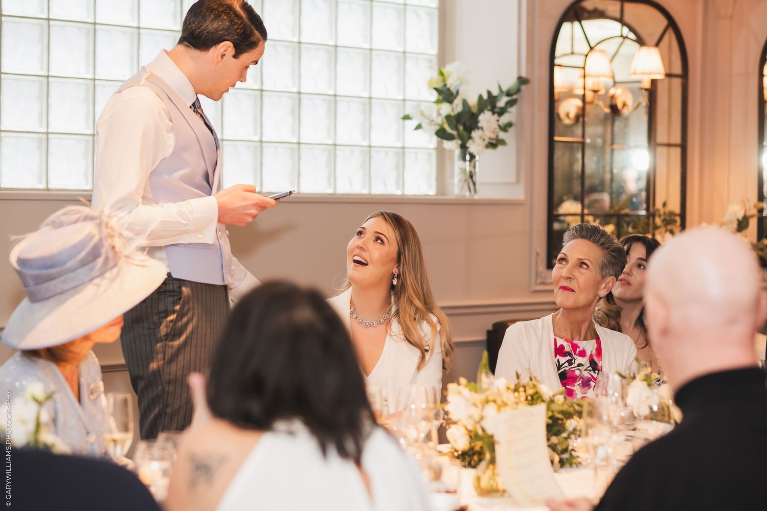 Wedding guests laugh and socialize during a reception dinner in an elegant dining room.