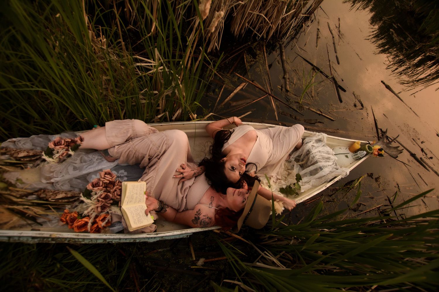 A figure in pale clothing lies in a small boat among reeds and tall grass at twilight.