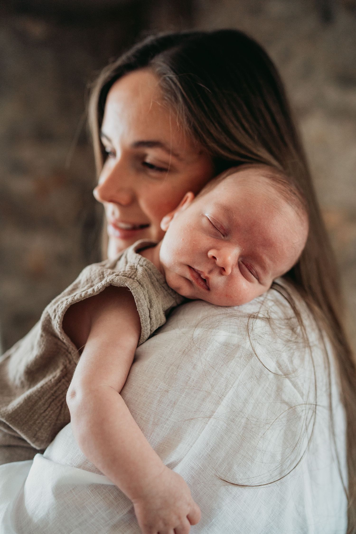 Mother in black dress lifts and kisses her happy child in pink dress at sunset in a rustic outdoor setting.