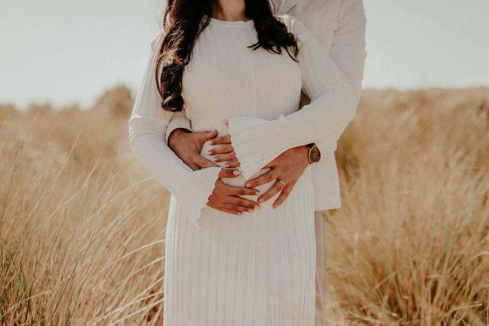 Couple holds hands intimately in a golden wheat field at sunset wearing white flowing outfits.