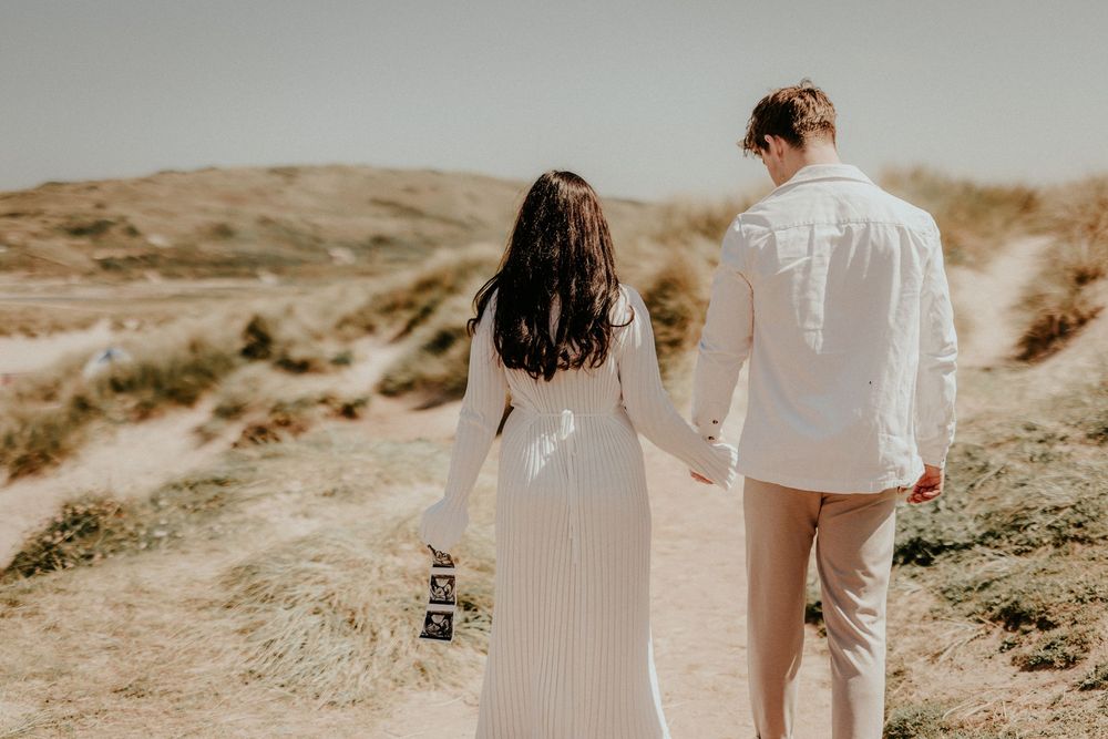 A couple in white clothing holding hands while standing on a hillside in golden afternoon light.