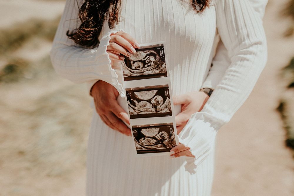 A series of maternity photos showing a white dress and ultrasound photos held against a pregnant belly outdoors.