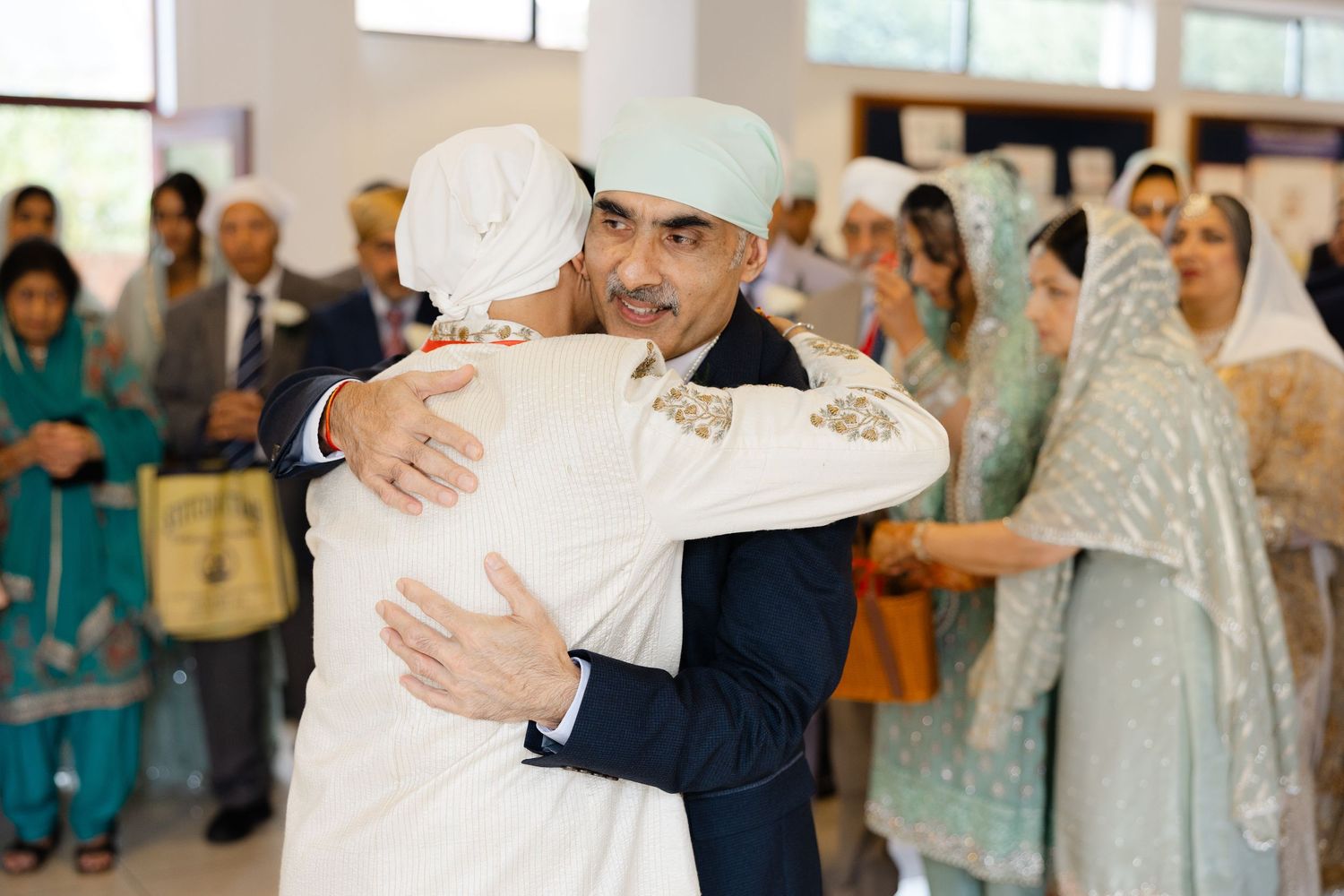 Bride and groom's fathers hug during Milni in Hounslow Gurdwara
