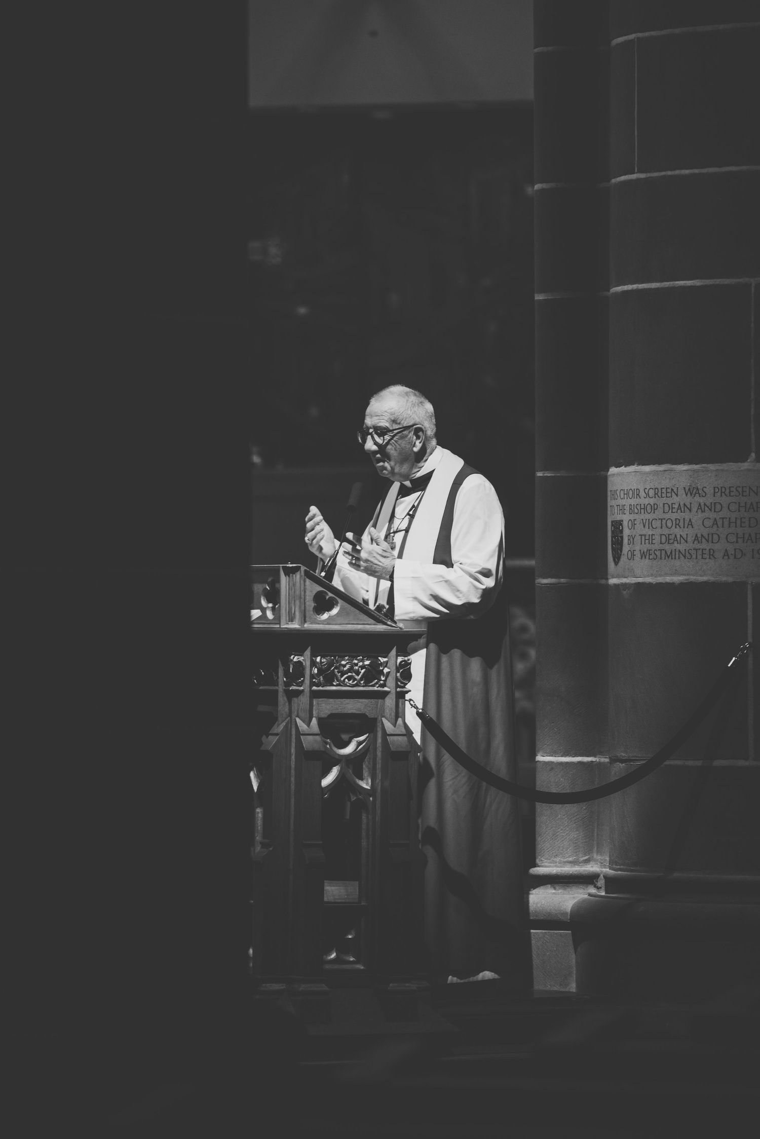 Black and white photograph of a clergy member in traditional vestments speaking from a church pulpit.