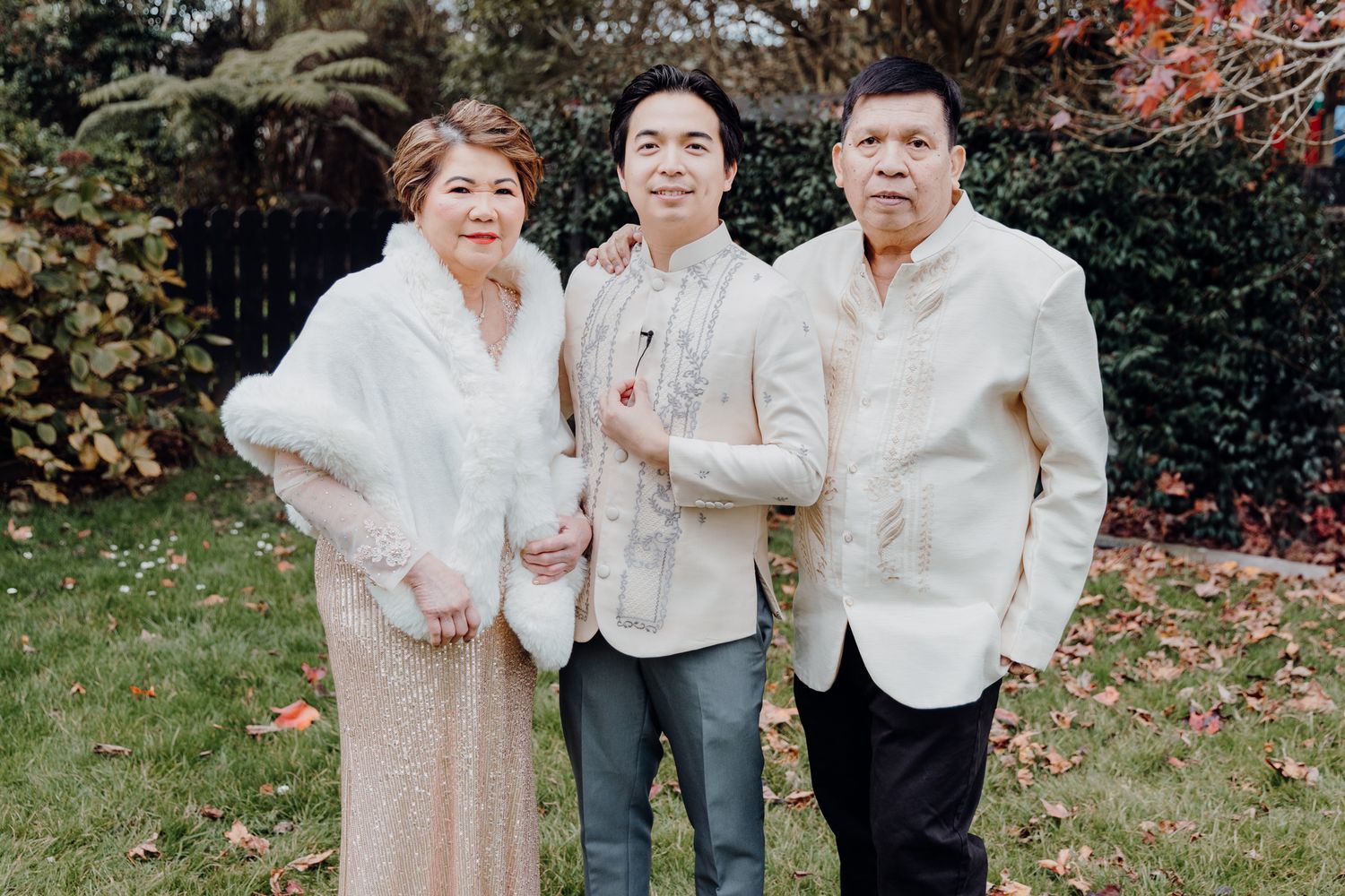 Family group wearing cream and white formal attire poses outdoors in autumn.