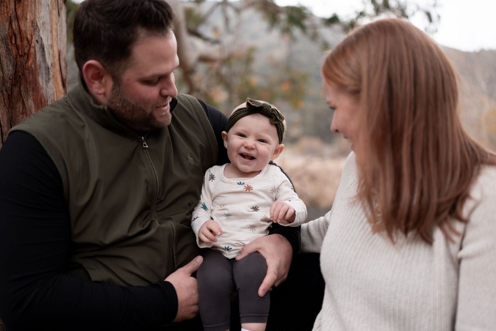 Intimate family moment captured outdoors as parents share loving smiles with their baby.