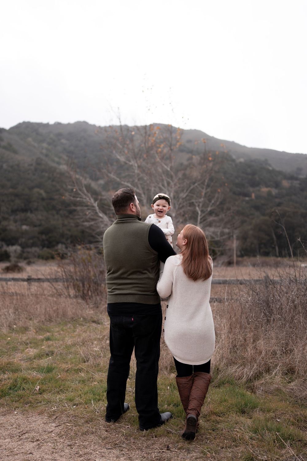 Family walking together on outdoor trail with mountains and bare trees in background.